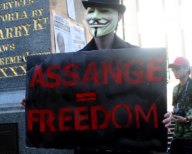 Anonymous protester holds up "Assange = Freedom" sign