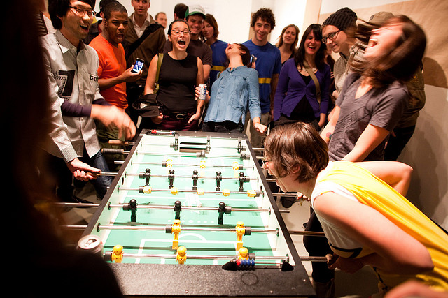 A bunch of people, who might be working at a startup, playing Foosball.