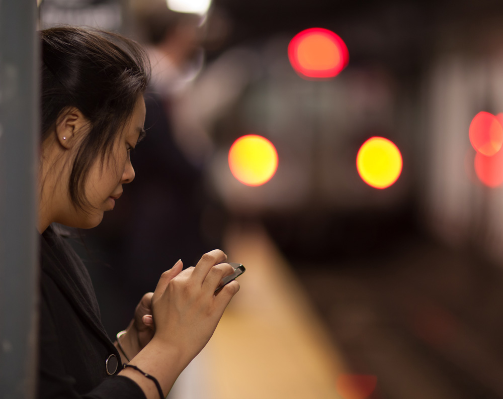 A woman uses her iPhone while waiting in a New York City subway station.