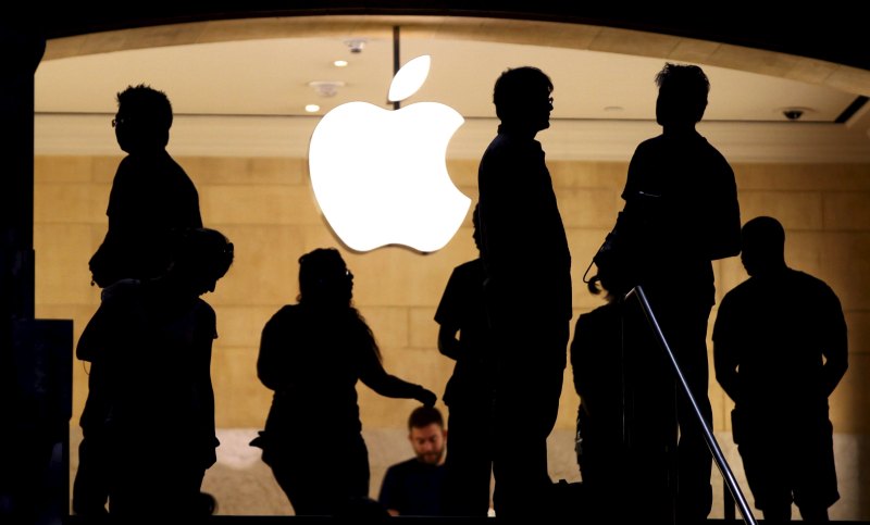 Customers stand beneath an Apple logo at the Apple store in Grand Central station in New York City, July 21, 2015.