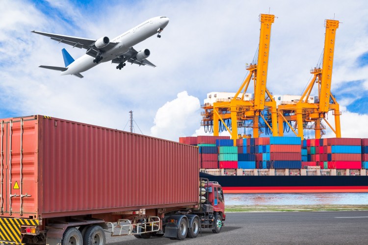 A truck pulls into a shipping port, with an airplane pictured overhead