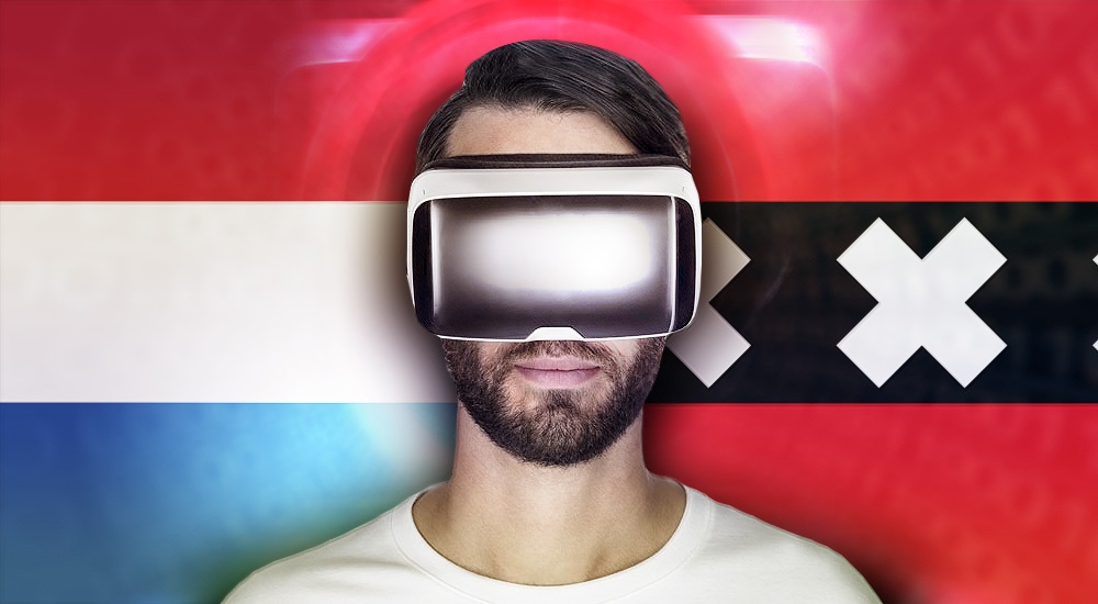 A man in virtual reality headset stands in front of a flag of The Netherlands.