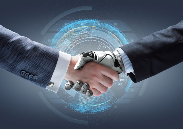 Artificial intelligence/robotics concept. Person's arm in suit shaking hands with robotic arm in suit.