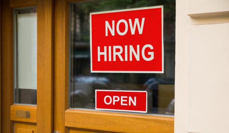 Picture of closed, dark office door with signs saying "now hiring" and "open"