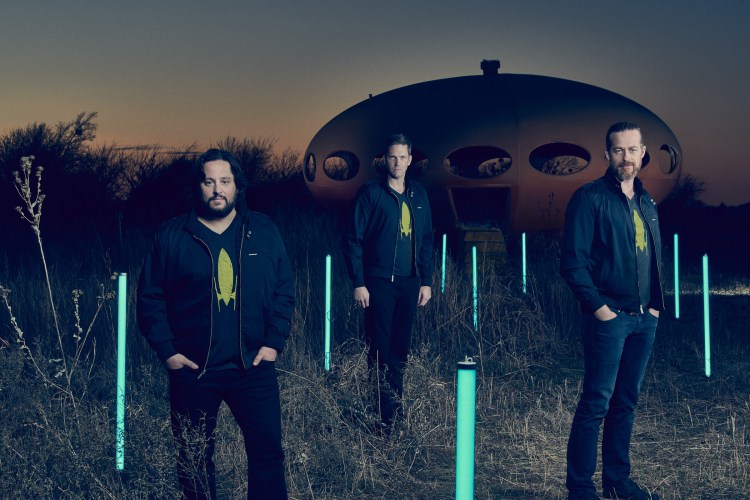 Three men stand in front of what looks like a spaceship.