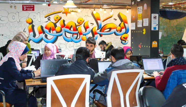People working at the Gaza Sky Geeks coworking space in front of graffiti that says “entrepreneurs" in Arabic.