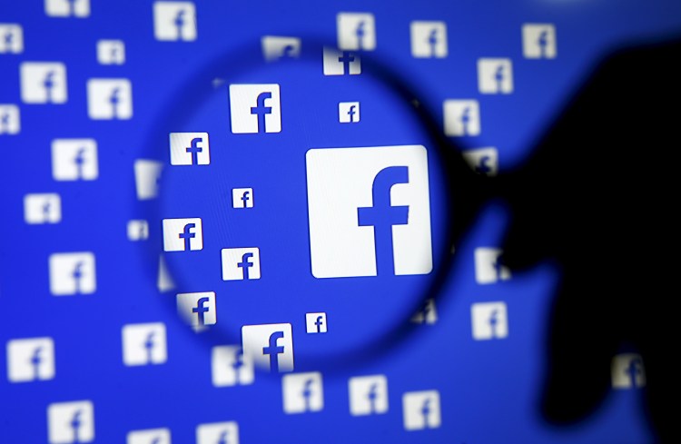 A man poses with a magnifier in front of a Facebook logo on display in this illustration.