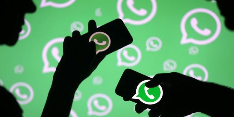 Men pose with smartphones in front of displayed Whatsapp logo in this illustration