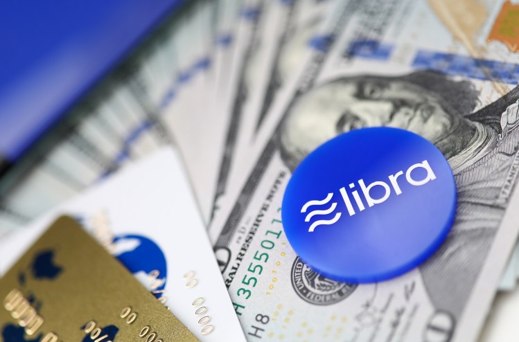 Blue chip with libra sign lying on big pile of US dollars and apps on cellphone in background close-up