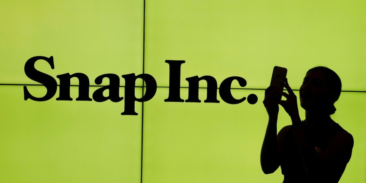 A woman stands in front of the logo of Snap Inc. on the floor of the New York Stock Exchange (NYSE) while waiting for Snap Inc. to post their IPO, in New York City