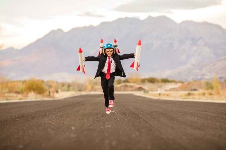 A young business boy in a rocket helmet and rockets in each hand is running for take off. He is breaking new ground as he launches his new ideas. His dream is to establish his own small business. This photograph was taken in Utah, USA.
