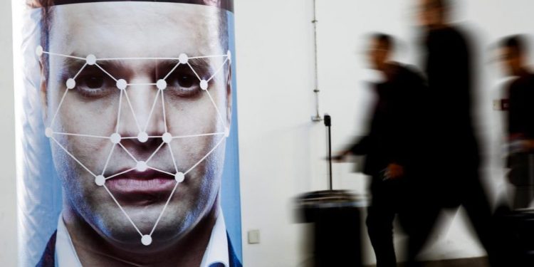 People walk past a poster simulating facial recognition software at the Security China 2018 exhibition on public safety and security in Beijing, China October 24, 2018. 