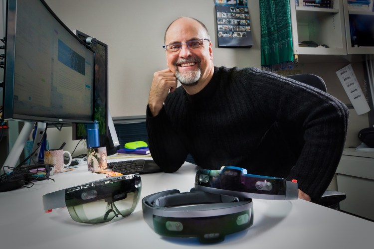 Ed Cutrell, a senior principal researcher with Microsoft’s research organization, sits behind several modified HoloLens units used by Project Tokyo researchers.