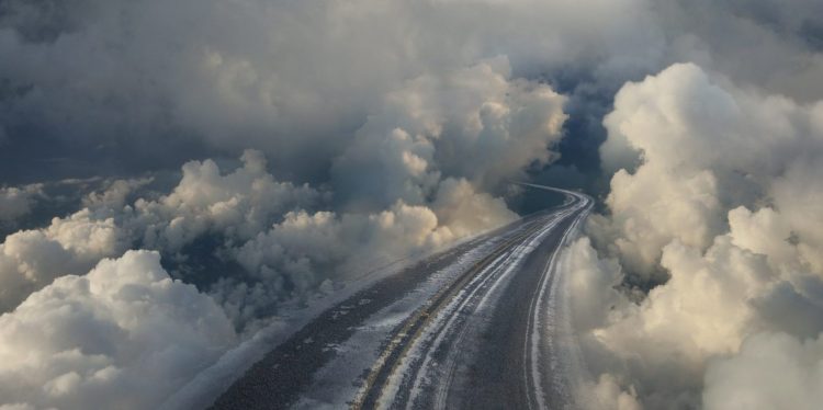 An empty highway curves off into clouds