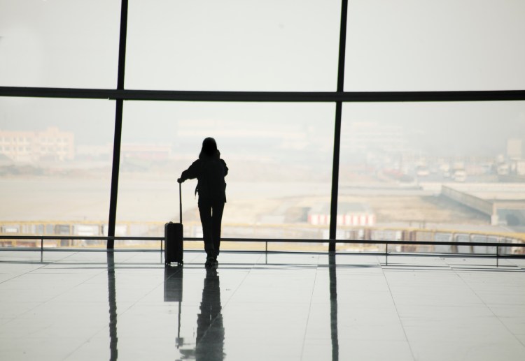 Silhouette of a woman with a suitcase at a large airport window