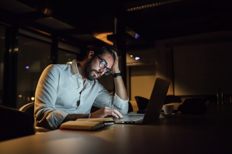 Stressed businessman in office at night working on laptop