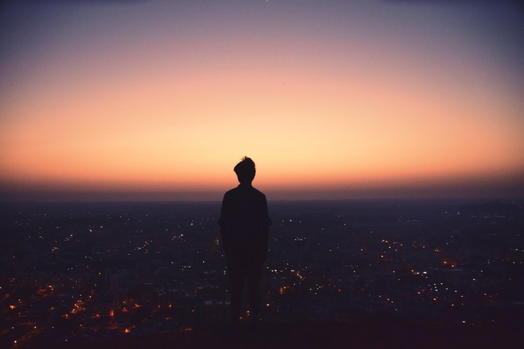 silhouette of a person on a hill top at dawn looking out over a city