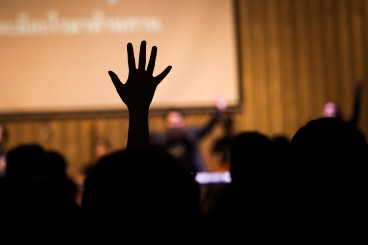 one hand is raised above heads of business people at a conference