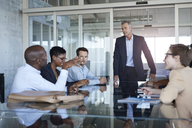 Business people dressed casual/corporate, talking together in large glass conference room
