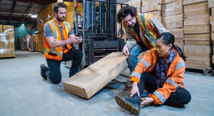An industrial warehouse workplace safety topic. A worker injured falling or being struck by a forklift.