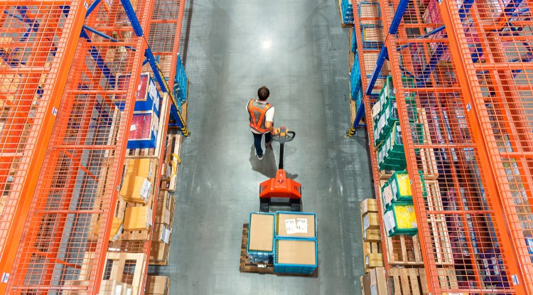 High angle view of warehouse worker pulling a pallet truck at distribution warehouse.