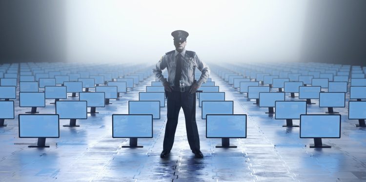 A security guard stands at the front of a roomfull of screens
