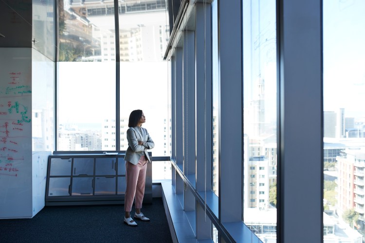 Businesswoman standing in corner of big office building and looking out of window