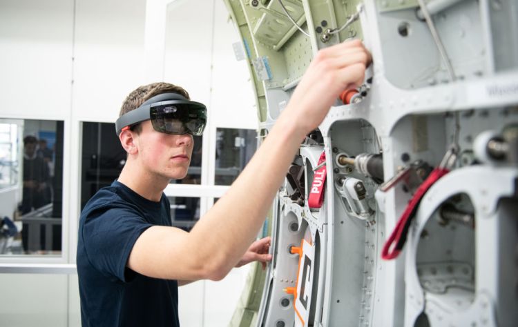 10 July 2019, Hamburg: During a demonstration, an Airbus trainee shows the use of data goggles (Microsoft Hololens) on an aircraft component. The spectacles work with the "Mira Mixed Reality" application developed by Airbus and are used, among other things, in maintenance and installation. At an event on the Airbus premises, the Hamburg Chamber of Commerce presented a position paper on digital education. Photo: Daniel Reinhardt/dpa (Photo by Daniel Reinhardt/picture alliance via Getty Images)