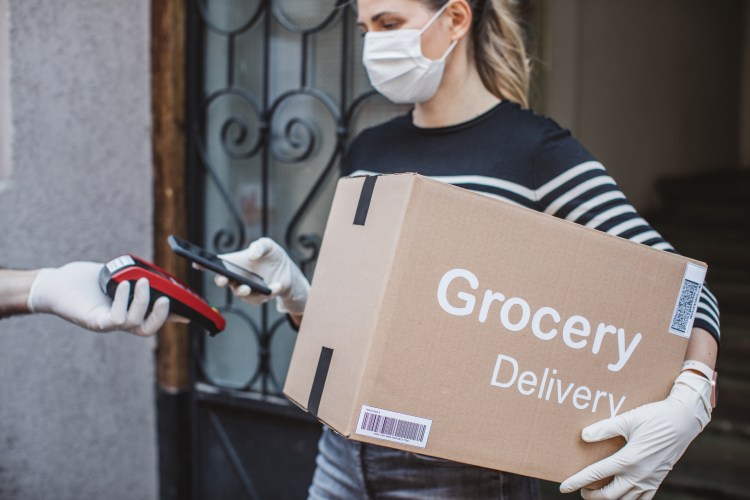Delivering food ordered online while in home isolation. Women taking over package and paying