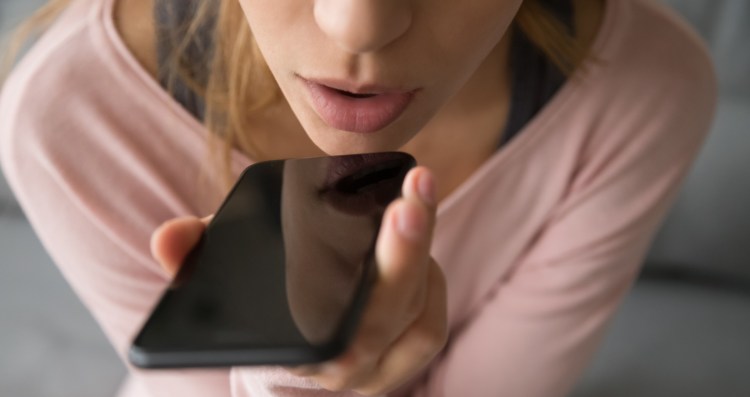 Close up girl sitting on couch hold on hand phone talk on speakerphone through microphone built into device loud reproduction of speech, voice recognition distant communication, translator app concept (Close up girl sitting on couch hold on hand phone