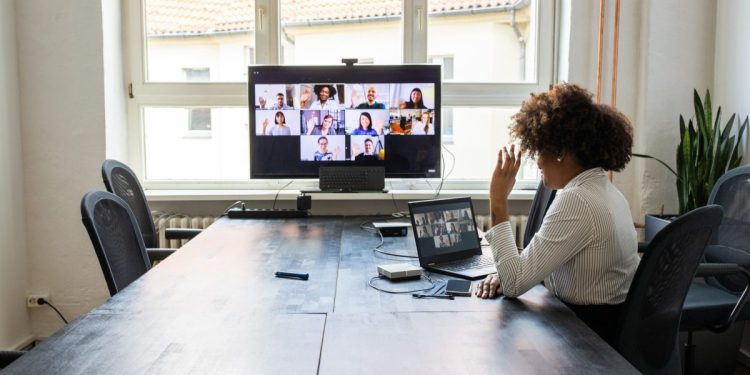 Rear view of a businesswoman having a meeting with team over a video conference in office board room. Meeting over a video call in office post pandemic lockdown.