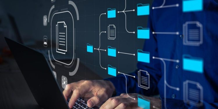 Document Management System (DMS) being setup by IT consultant working on laptop computer in office. Software for archiving, searching and managing corporate files and information. Business processes