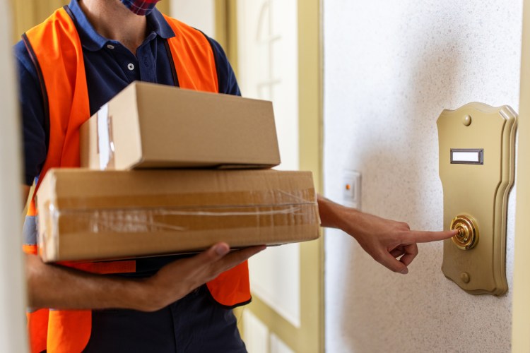 Cropped shot of a male courier delivery person holding parcel boxes and ringing doorbell. Postal worker doing a home delivery of parcel.