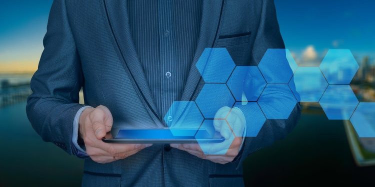 Graphic of a businessperson holding a tablet with hexagons coming out of it. A city in the background.