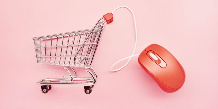 Still life of a small shopping cart and red computer mouse on pink background