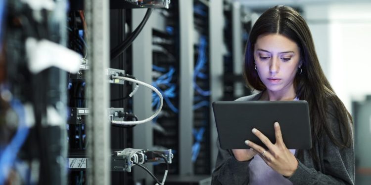 Female technician using digital tablet in server room. IT professional is standing at workplace. She is in casuals.
