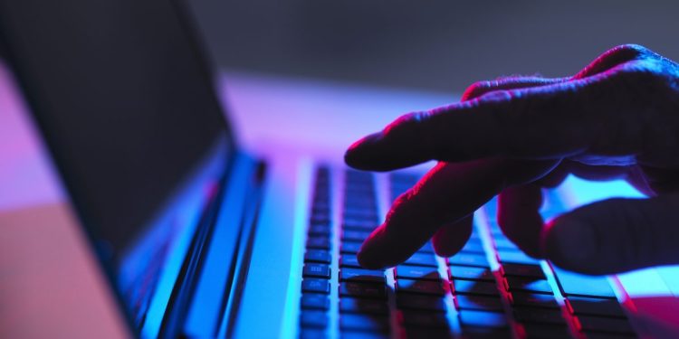 Silhouette of male hand typing on laptop keyboard at night