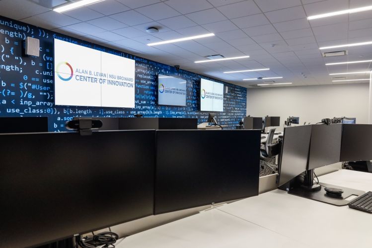 The cyber range at Alan B. Levan / NSU Broward Center of Innovation, a wall of monitors in front of desks covered with large desktop monitors