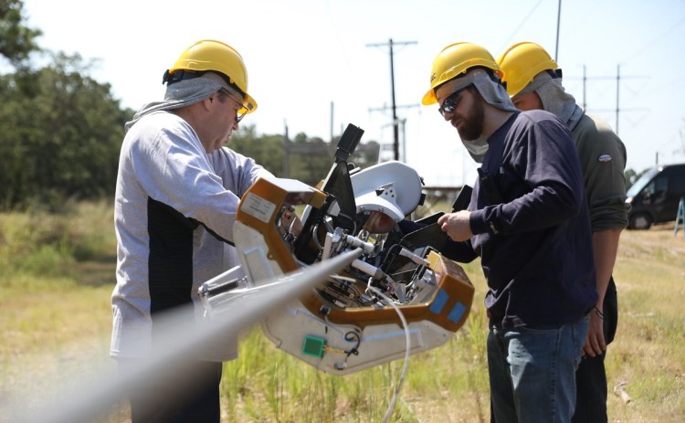 Technicians attach Facebook's Bombyx robot to a telephone wire.