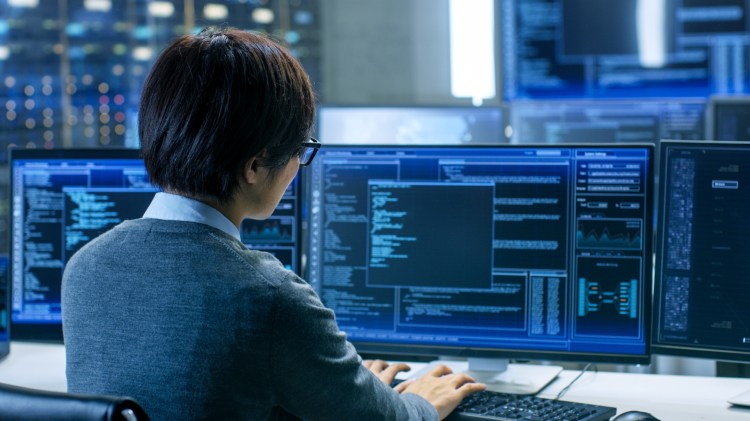 In the System Control Room Technical Operator Works at His Workstation with Multiple Displays Showing Graphics. IT Technician Works on Artificial Intelligence, Big Data Mining, Neural Network Project.