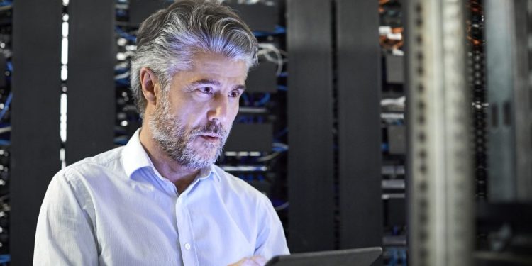 Engineer with digital tablet examining in server room. Male IT professional is working at workplace. He is in casuals.