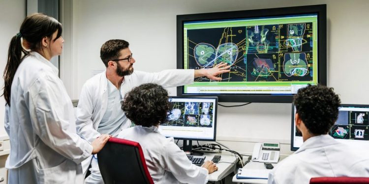A group of clinical doctors discussing a patient's test results on a large monitor in an office using consumer healthcare data.