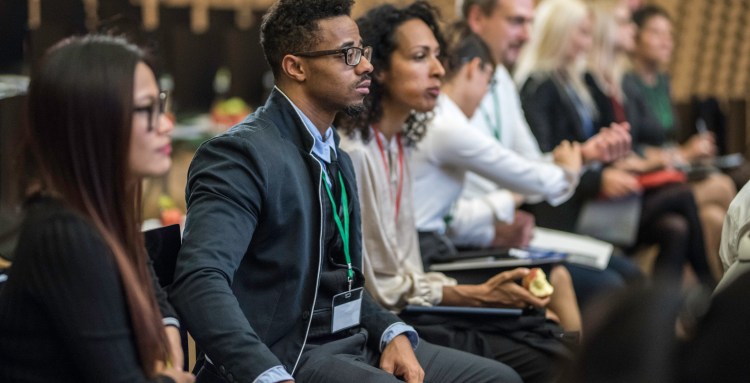 Close up side view of a group of multi-ethnic people sitting in chairs listening to a lecture at a conference.