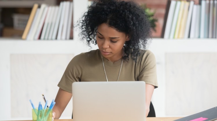 Busy serious African American businesswoman working with laptop and documents in office, check finances, writing report, focused student studying in library, writing notes, distance learning online