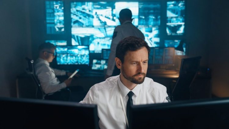 An employee of security, security, police, rescue service, FBI, CIA, sits at his workplace behind monitors. The man works behind two monitors, he studies the received information.