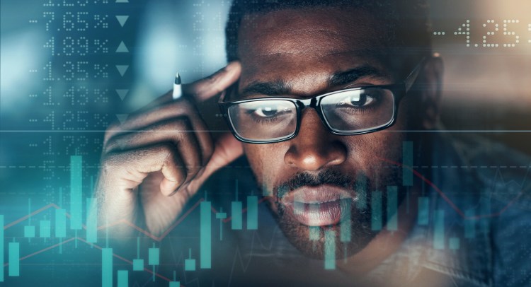 Shot of a young businessman looking worried while using a computer during a late night in a modern office