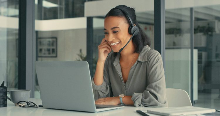 Shot of a young woman using a headset and laptop in a modern office for virtual sales experience