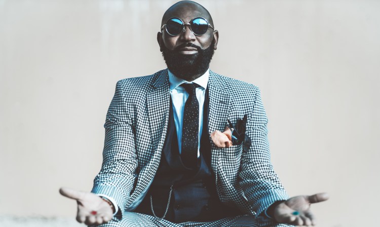 A concept photo with an elegant bald bearded man in a suit with tie and round sunglasses offering to make a choice with red and blue pills in his hands