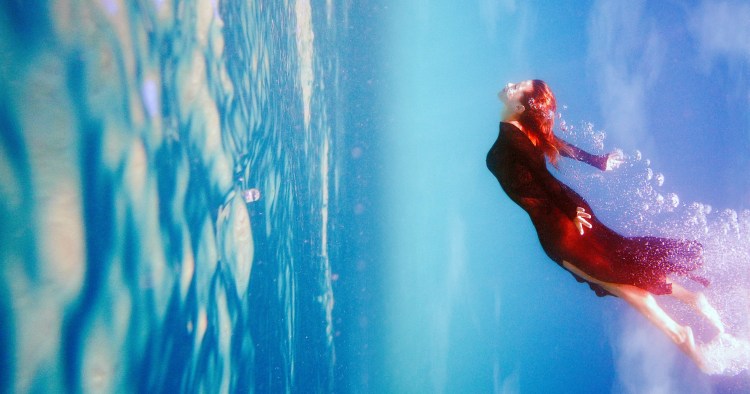 Journey into the unknown.  Woman in red dress emerges and air bubbles are around her. Underwater photo.