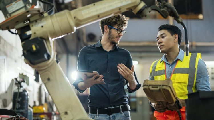 Software engineer and mechanical parts manufacturer discussing in factory setting